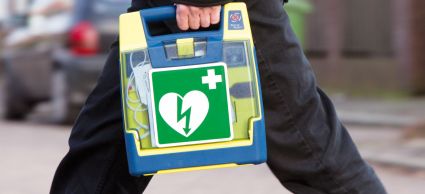 Foto van een persoon die een AED draagt en over straat loopt